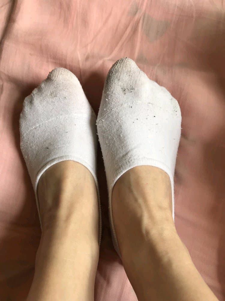 Close-up of bare Asian feet resting on satin, toes slightly curled, stocking sheen and soft warm lighting