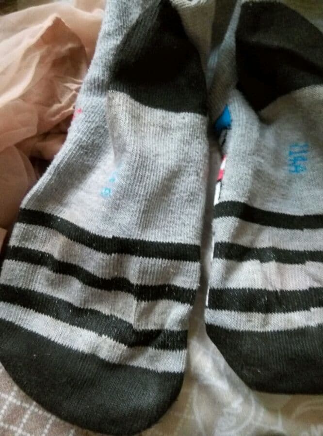 Feet dipping into shallow water with sheer nylon clinging and droplets highlighting the curves of toes and arches.