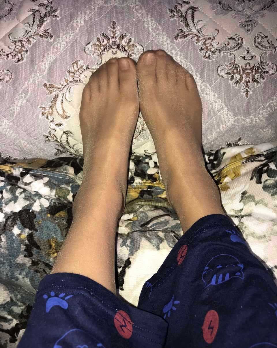 Cuffed pants slightly raised to reveal sheer tights beneath, leg extended to show nylon sheen and ankle line