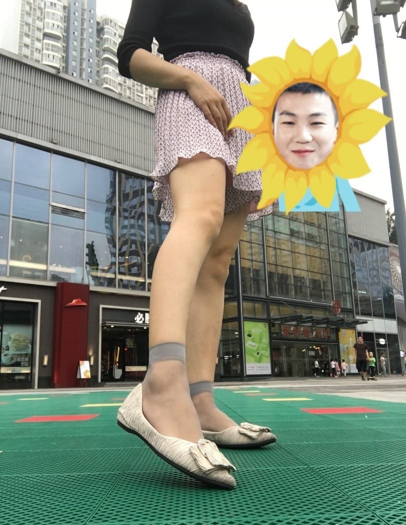 Model resting foot on curb in city light, stocking hem rolled and toes peeking, urban shop window backdrop