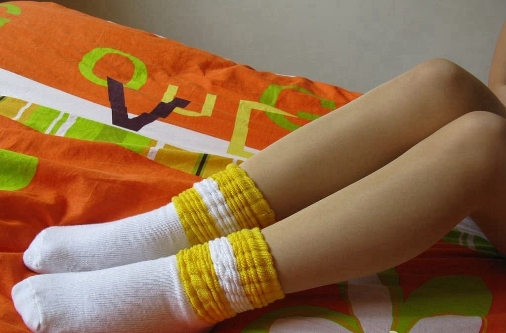 Two pairs of feet in close proximity, one in nylon stockings and the other with worn cotton socks casually removed