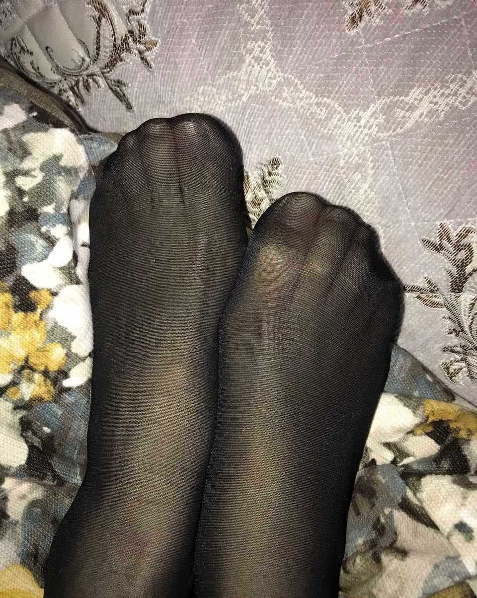 Elegant foot in black stockings, toes peeking from sheer fabric with a soft-lit shadowed background