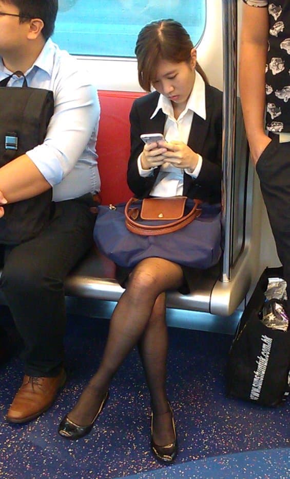 Woman in black stockings and white collar seated on subway, legs crossed, nylons gleaming under fluorescent lights, evocative mood