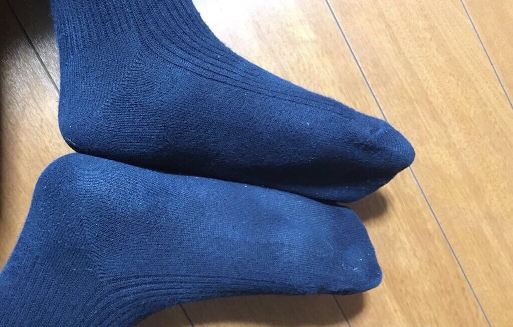 Adult model wearing knee-high ribbed socks with slight wear, legs crossed in playful pose