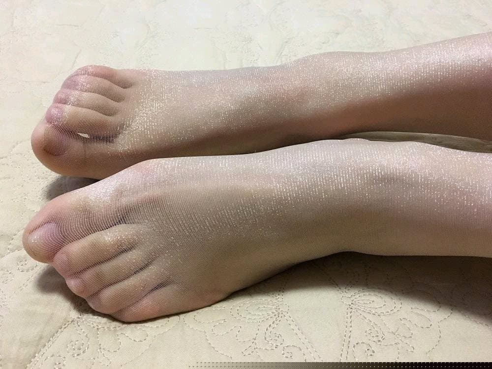 Soft-focus close-up of small bare feet with painted toenails, toes relaxed and arches slightly raised on a plush blanket