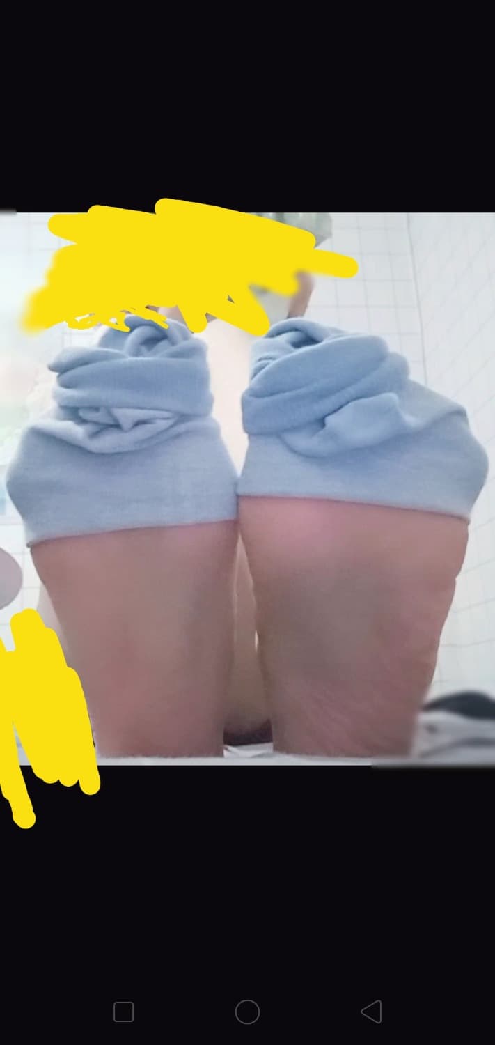 Overhead shot of delicate barefoot arches slipping into glossy stockings, ankle straps and smooth skin in warm light