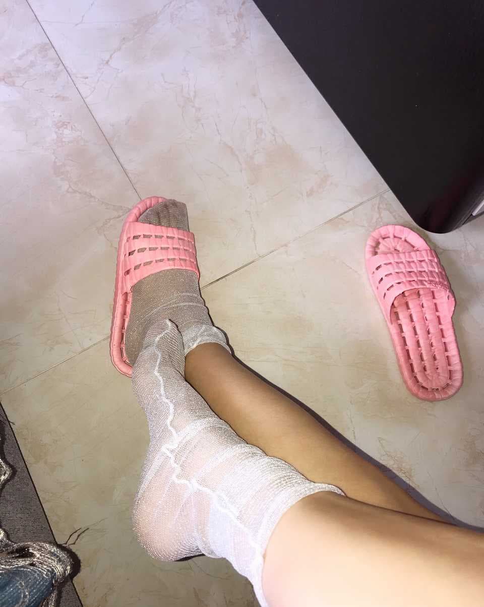 Legs in glossy white pantyhose stretched out on a sunlit chaise, toes gently flexed beneath fabric