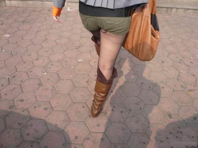 Full-length street shot showing torn black stockings, frayed runs revealing patches of skin along the leg