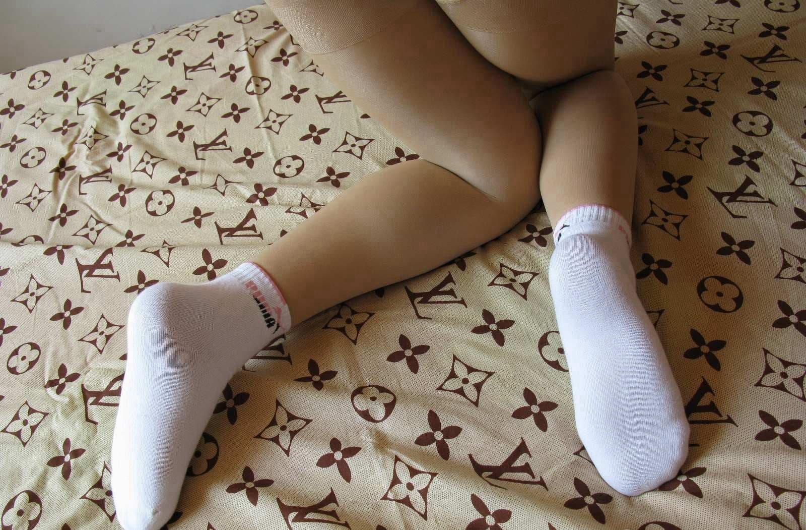 Pair of white cotton socks and delicate sheer stockings arranged on a luxury LV-patterned bed sheet