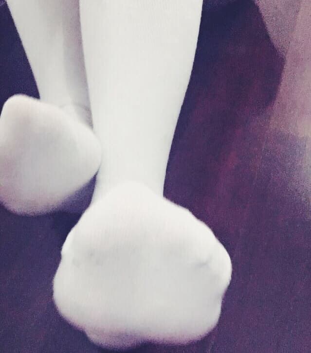 Close-up of bare feet slipping into sheer black stockings on a bed with soft, warm lighting