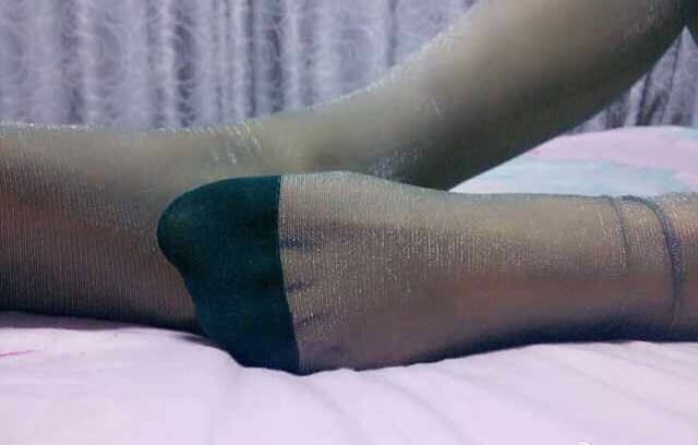 Close-up of glossy nylon-clad foot arch and curled toes in soft studio light, sheen highlighting every curve and seam.