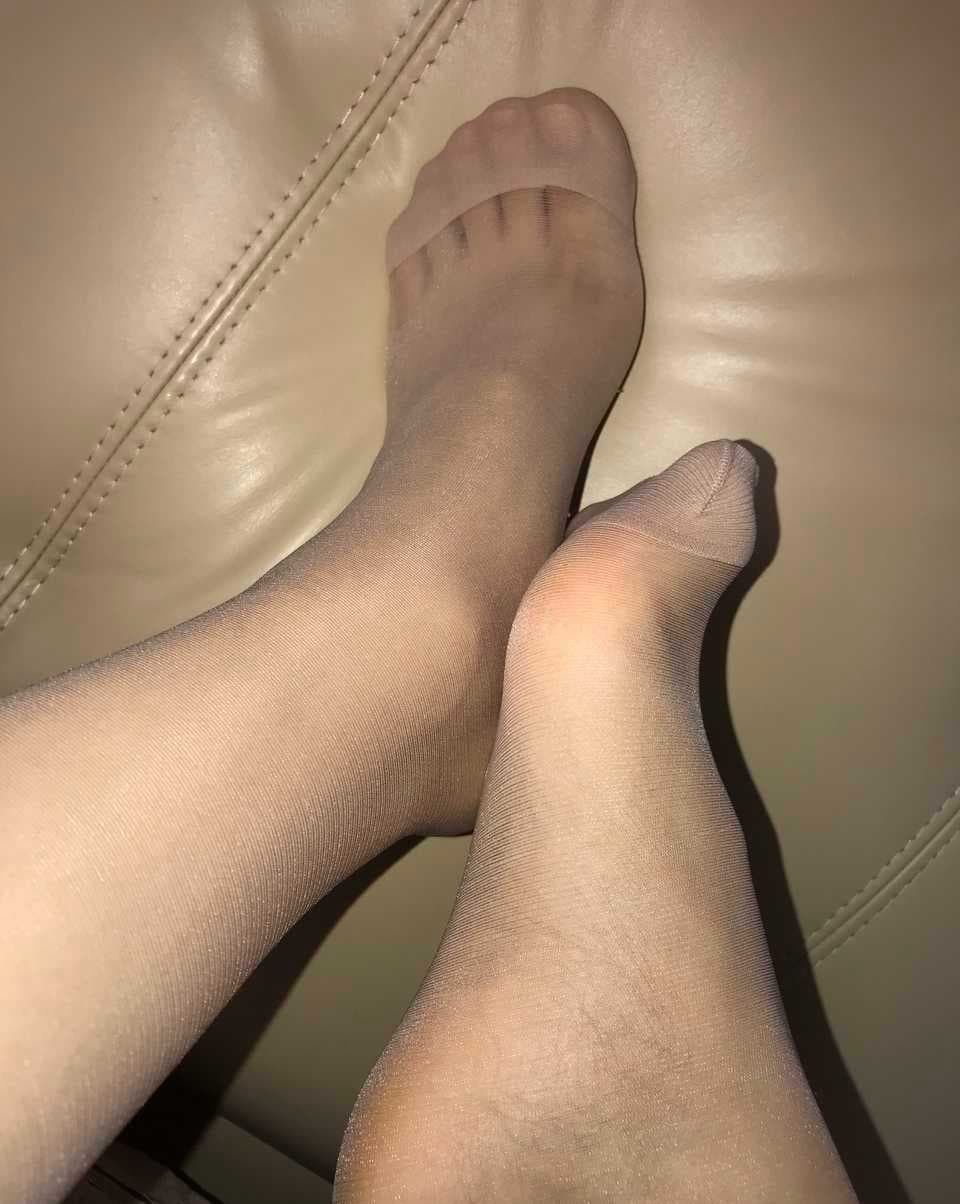 Relaxed sofa scene with legs in flesh-toned stockings, feet resting on plush cushions in warm light