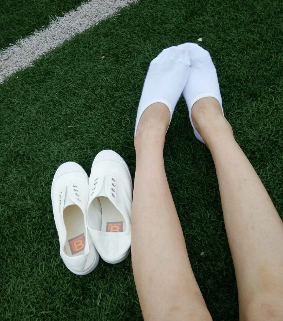 Pair of small cloth shoes beside a barefoot with curled toes, showing fabric creases and intimate domestic warmth.