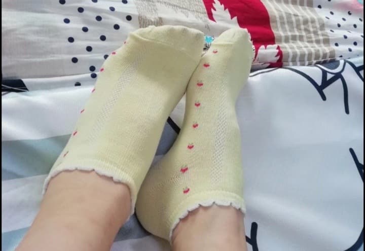 Slightly worn cotton socks scrunched at ankles on bed sheets, hinting at scent and intimacy