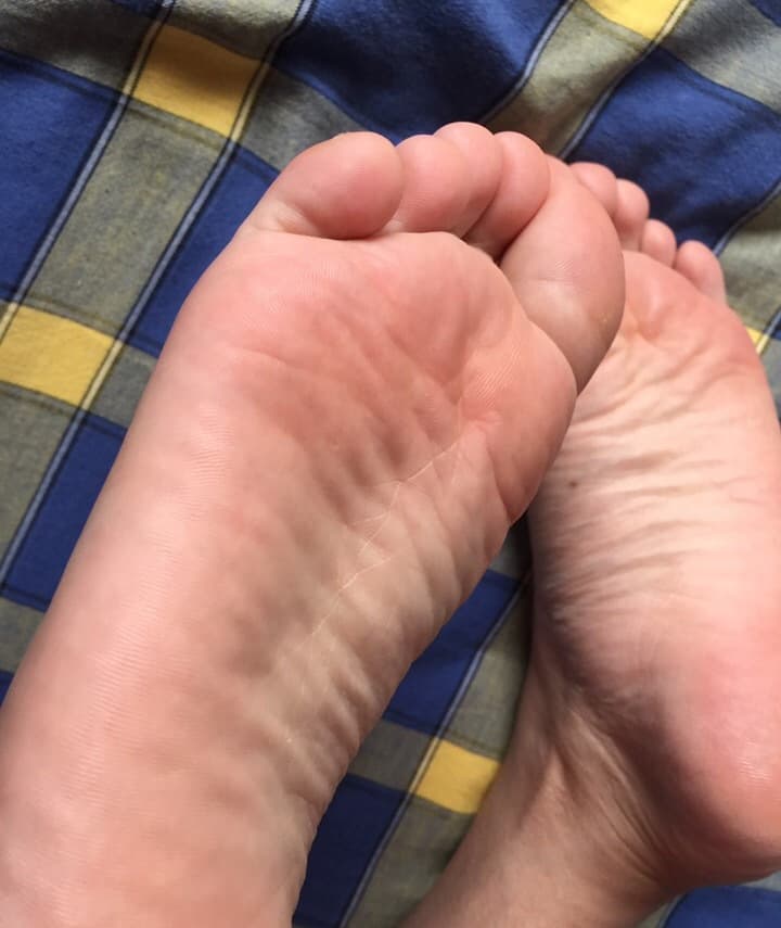 Intimate close-up of small, bare feet resting gently, toes slightly splayed and soft skin catching warm light