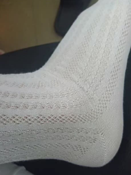 Adult feet side by side with one hand reaching toward a nylon-clad arch, creating a teasing, consensual moment