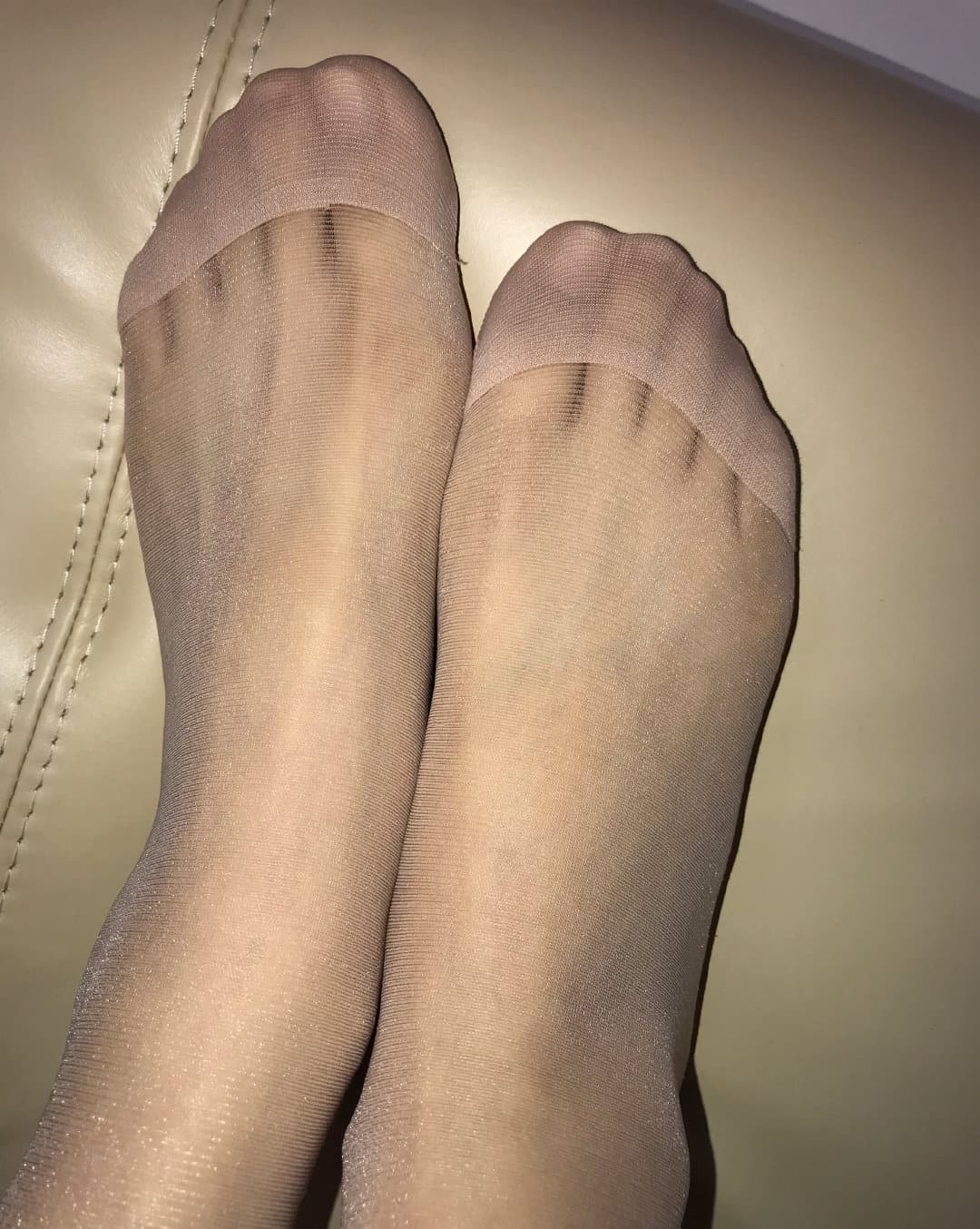 Bare feet draped over a sofa cushion, relaxed toes and soft soles highlighted in warm light