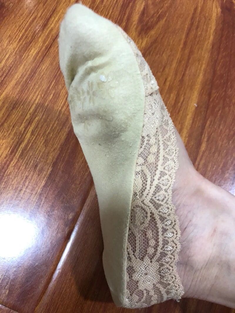 Two feet side by side, one stockinged and one bare, posed invitingly on soft fabric