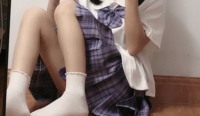 Adult model in a JK-style uniform with sheer knee-highs, sitting with one leg crossed and ankle exposed