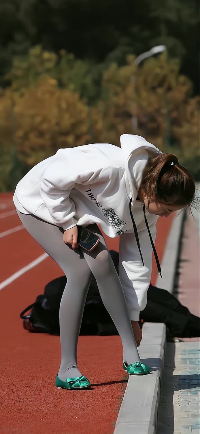 Feet peeking from beneath a skirt, grey nylon catching campus sunlight in warm tones