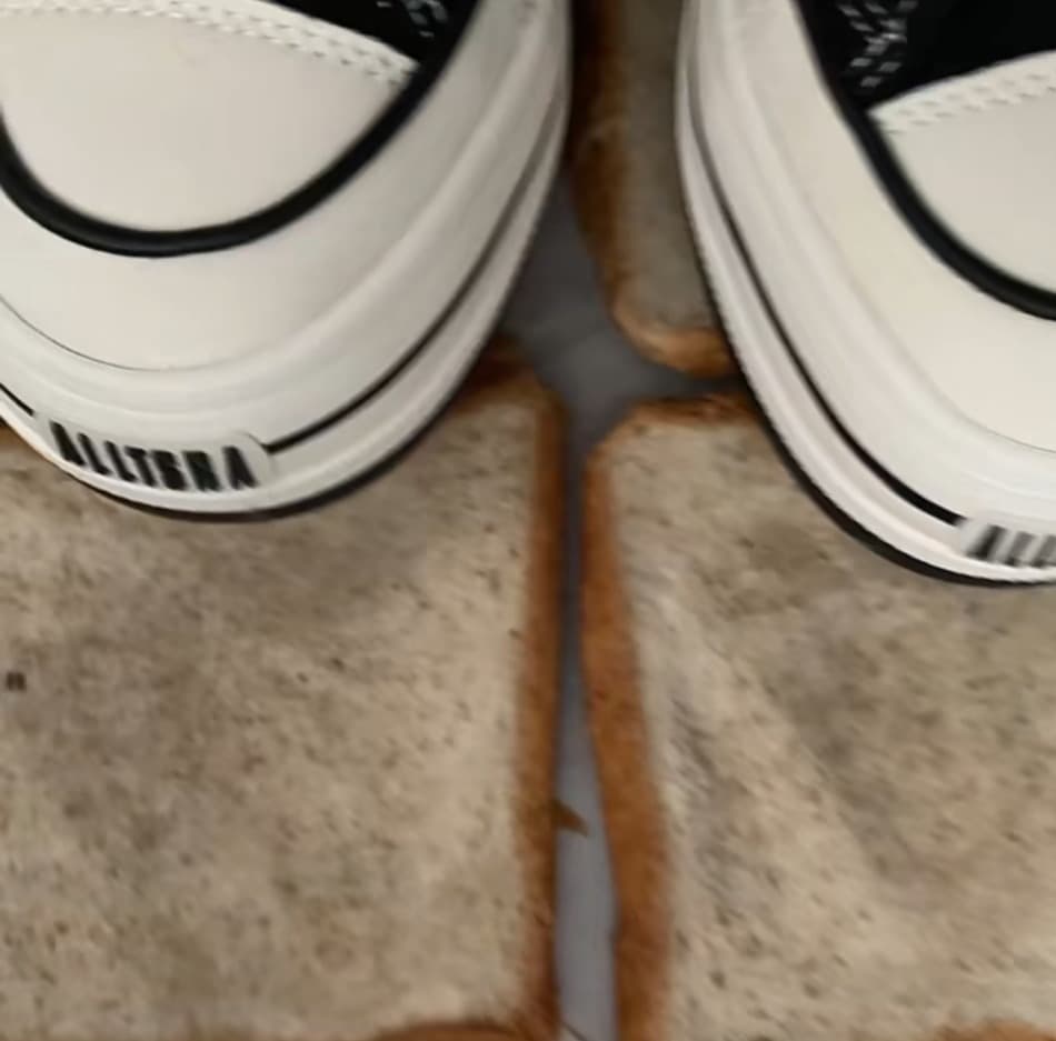 Close-up of bare feet stepping onto ripe fruit, nylon sheen visible, toes curling against textured surface in warm, intimate lighting